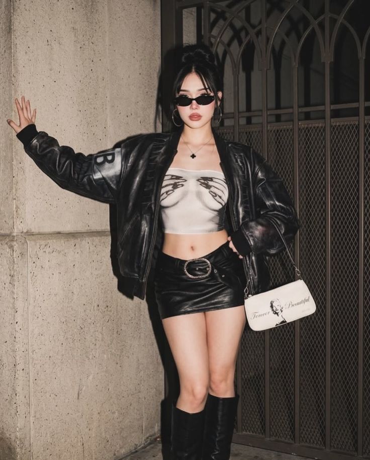 Woman in a leather jacket and mini skirt posing against a wall