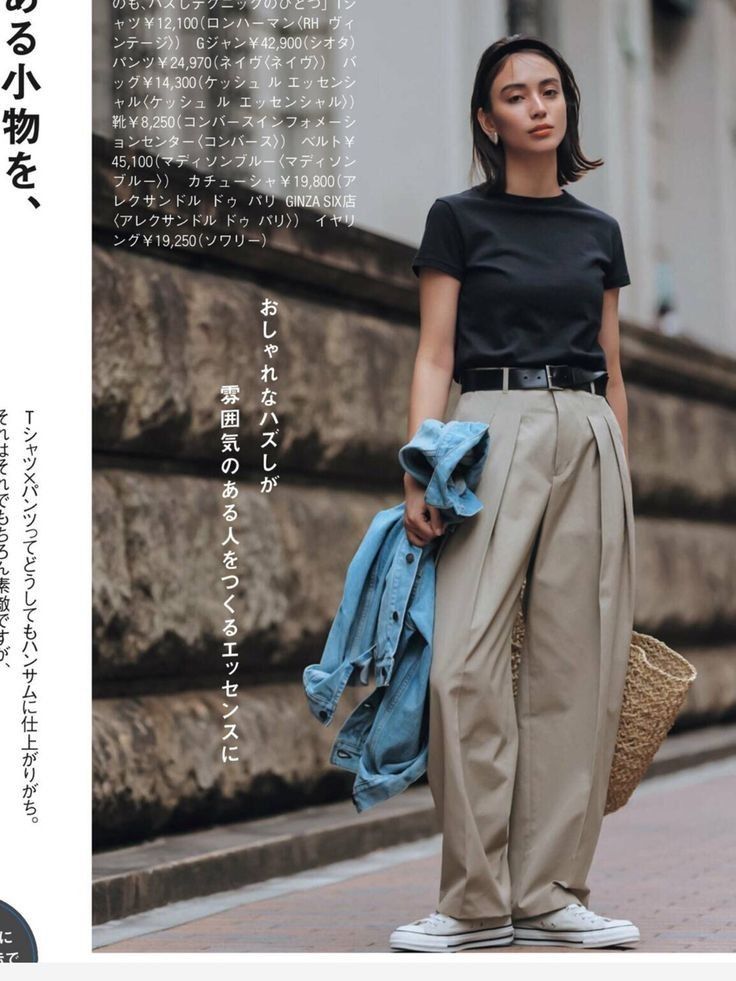 Woman in a black t-shirt and khaki pants holding a denim jacket and straw bag