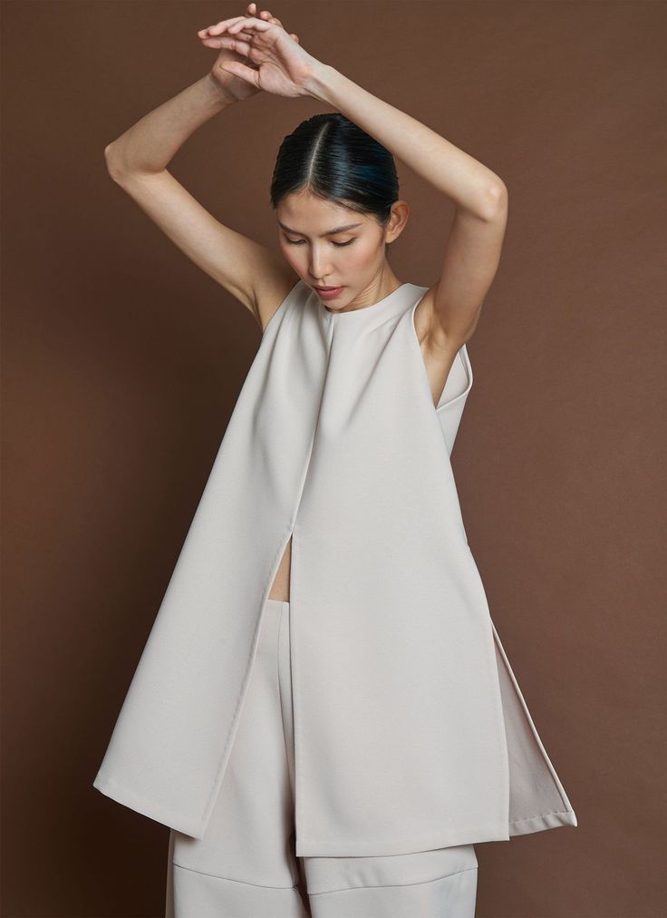 Woman in a light-colored sleeveless top with a split front and high neck