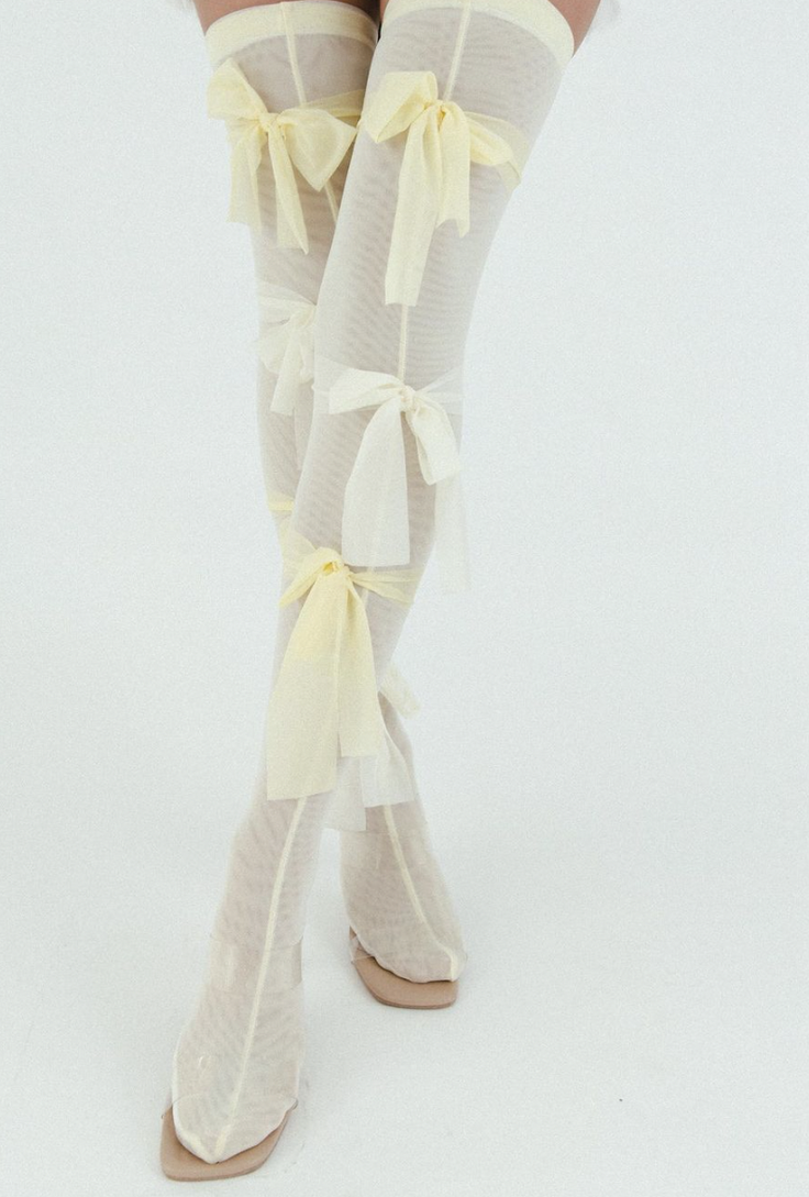 Legs wearing sheer thigh-high stockings with yellow bows and square-toe shoes
