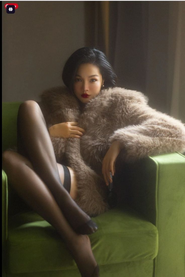 Woman in a fur coat and stockings posing on a green couch