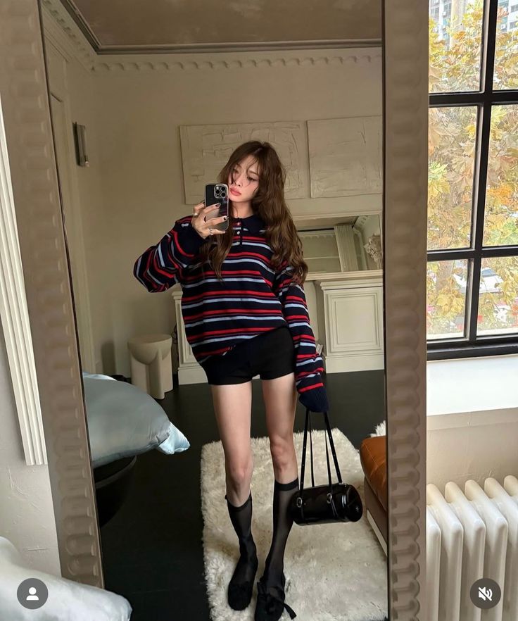 Woman in a striped sweater and black shorts taking a mirror selfie indoors