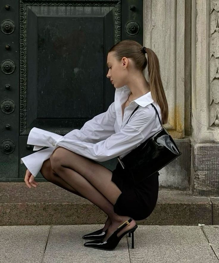 Woman in a white shirt and black skirt crouching outdoors