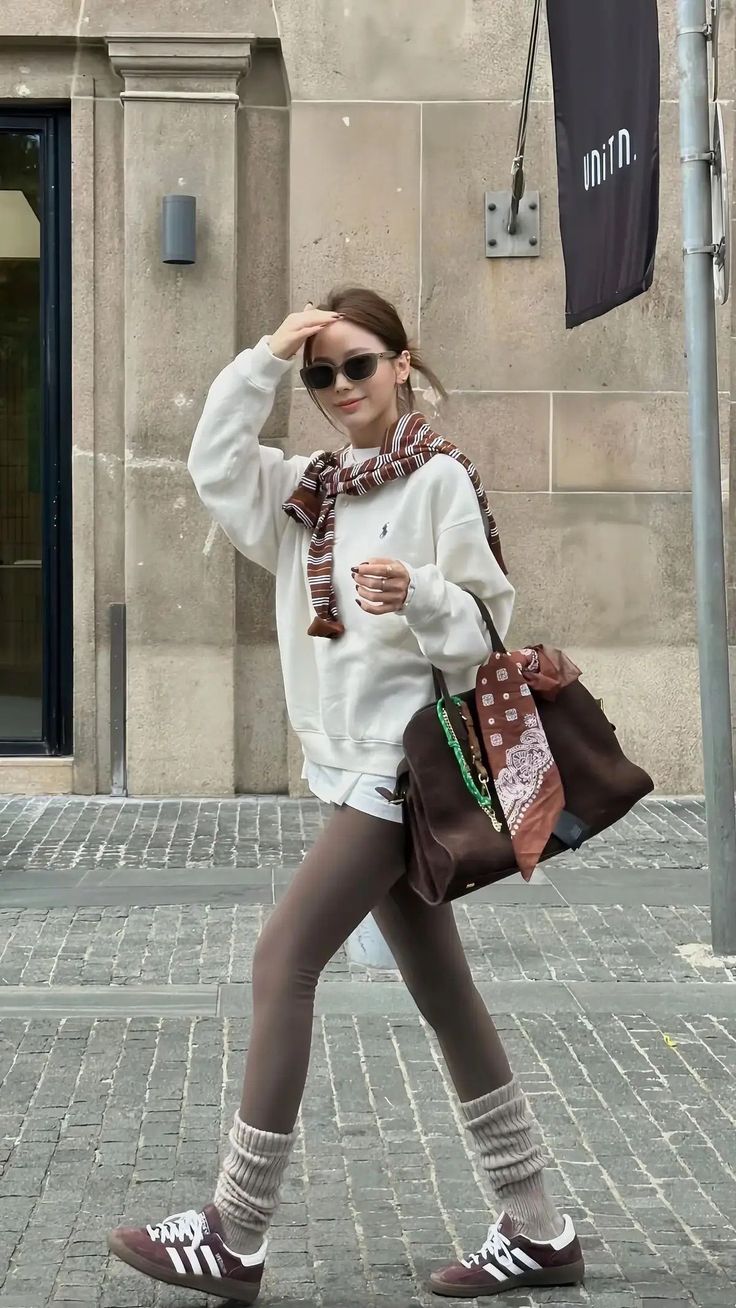 Woman in a white sweatshirt and brown leggings walking on a street