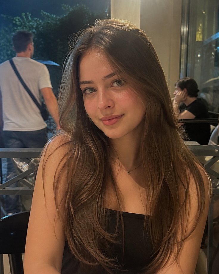 Young woman with long brown hair wearing a black top indoors at night