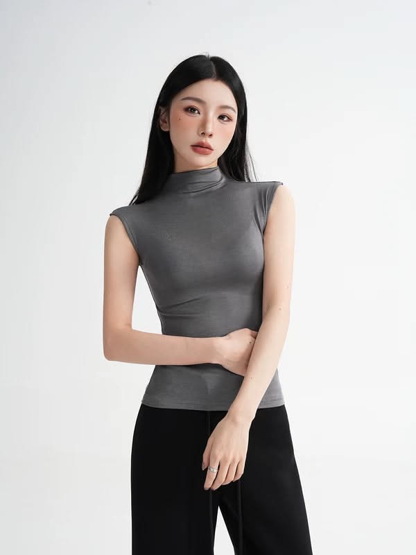 Woman with long black hair wearing a gray top and black pants in a studio
