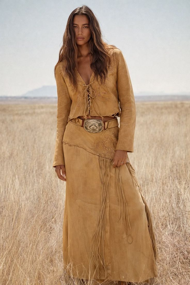 Woman in a suede outfit with a western belt standing in a field of dry grass