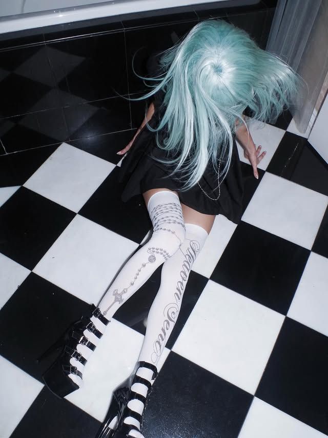 Person with blue hair and a black dress lying on a checkered floor