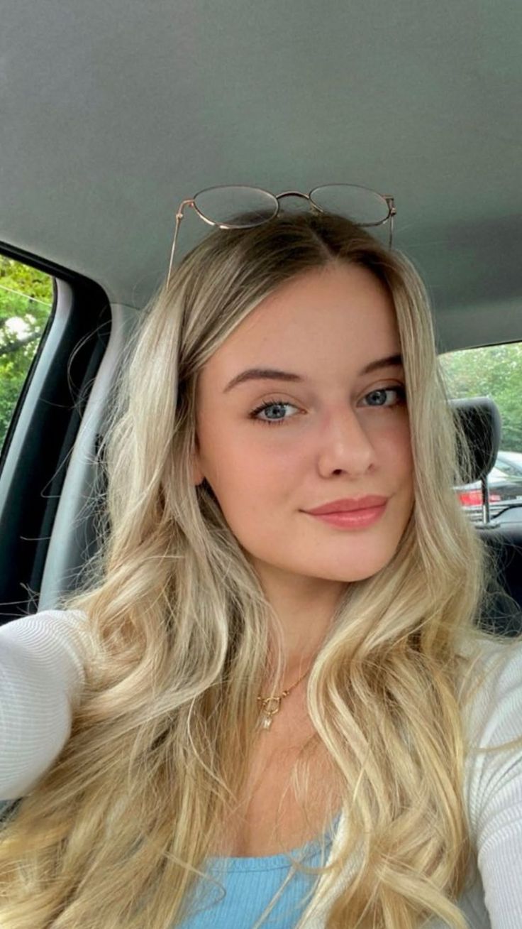 Blonde woman with glasses on her head and a gold necklace in a car
