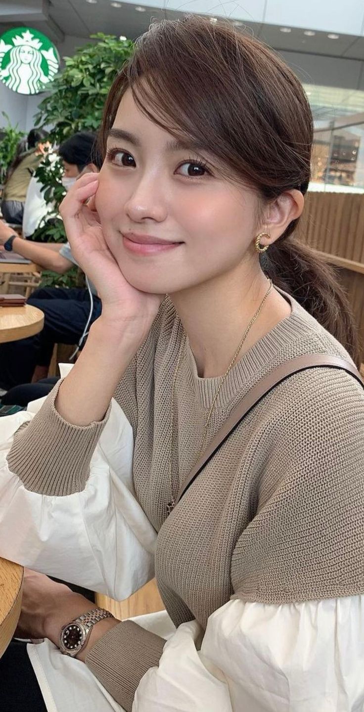 Woman with brown hair in a sweater, smiling and resting her chin on her hand