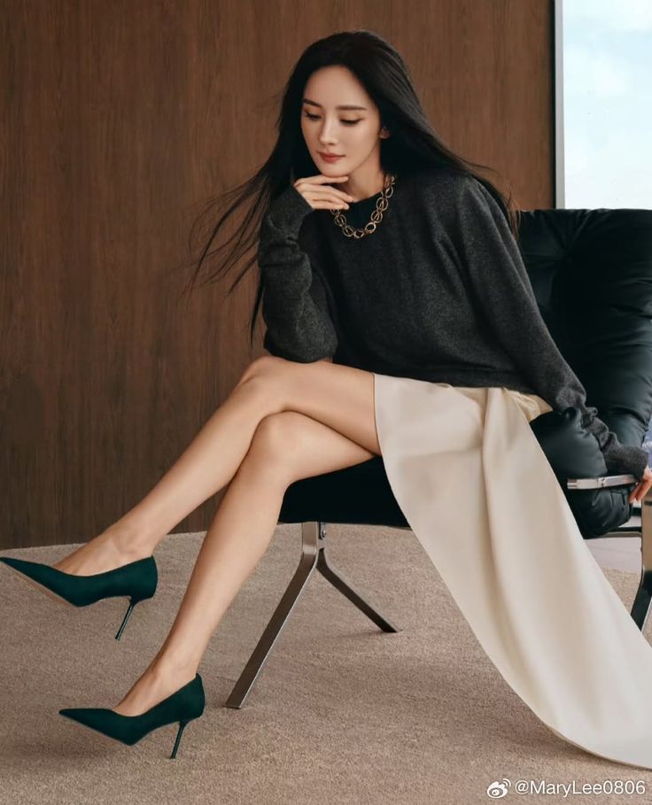 Woman with long dark hair wearing a sweater and high heels, sitting indoors