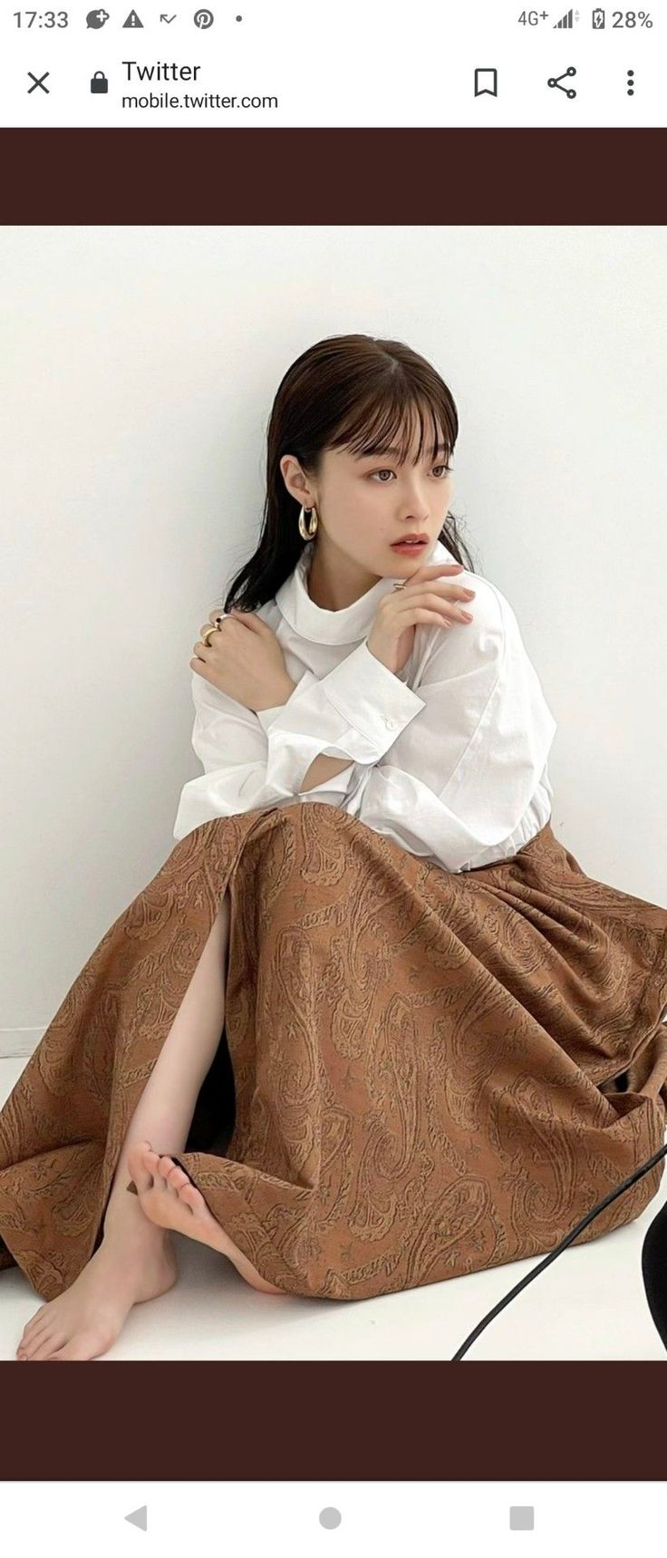 Woman with long hair wearing a white shirt and brown skirt, sitting indoors