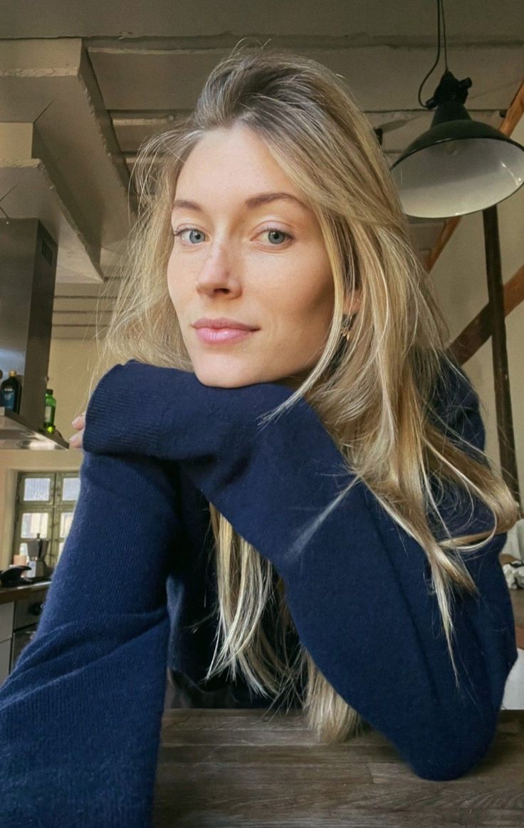 Woman with long blonde hair and blue eyes wearing a navy blue sweater indoors