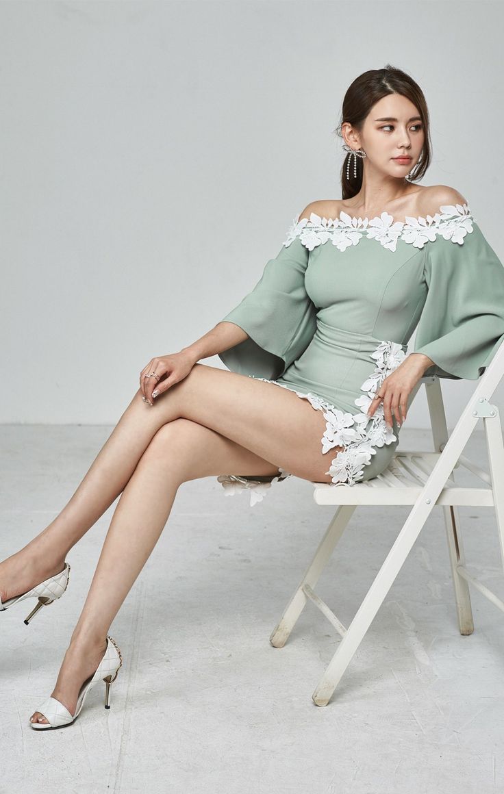 Woman in a light green off-shoulder mini dress with white floral details, sitting on a chair
