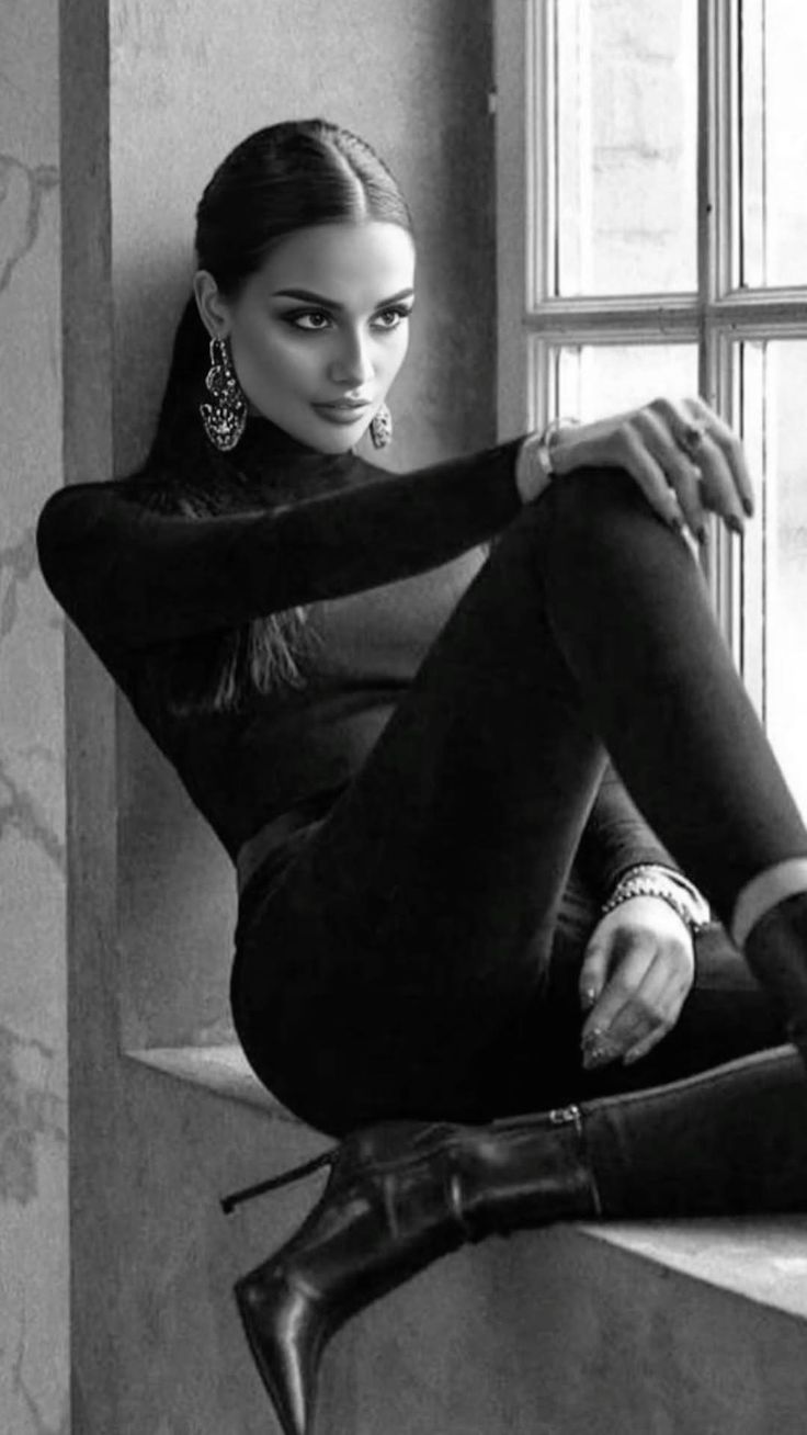 Woman in a black turtleneck and high heels sitting by a window