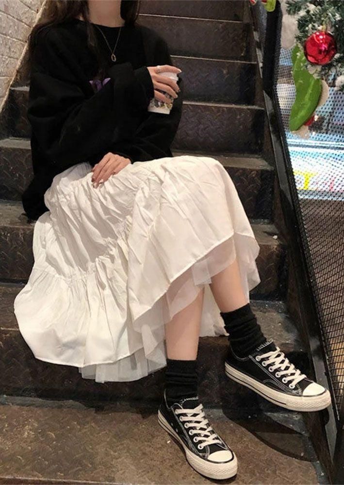 Person in a black sweatshirt and white skirt sitting on stairs