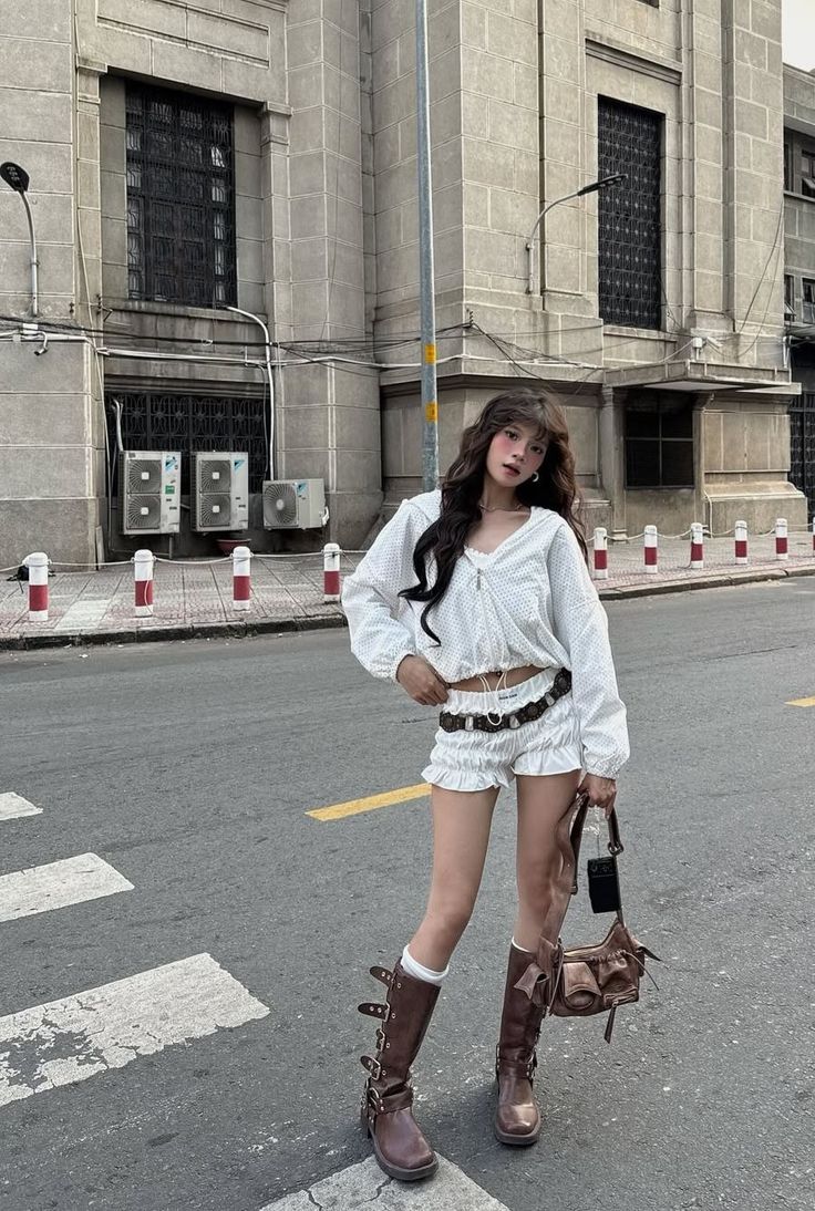 Woman in white top and shorts with brown boots standing on a street