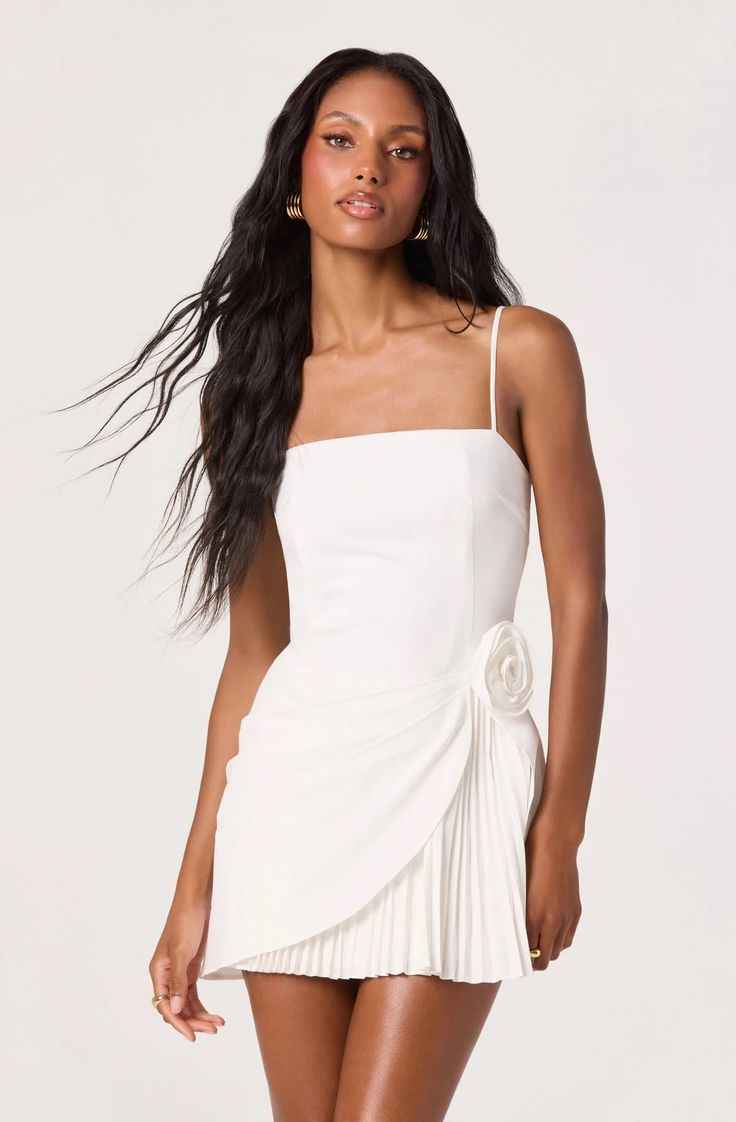 Woman with long dark hair wearing a white dress with a floral detail