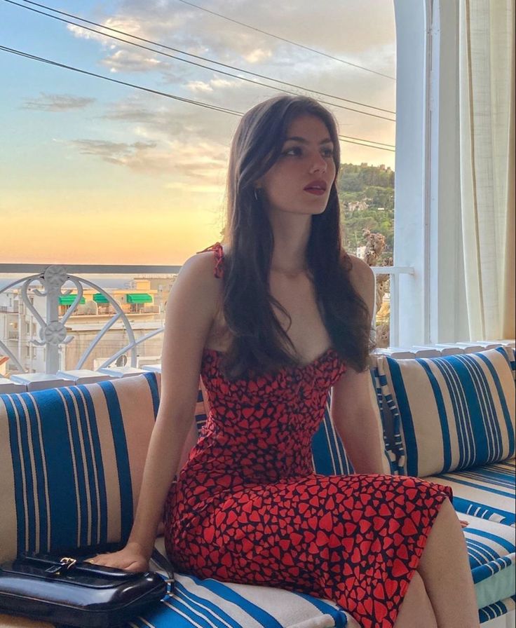 Woman in a red heart-patterned dress sitting on a balcony at sunset