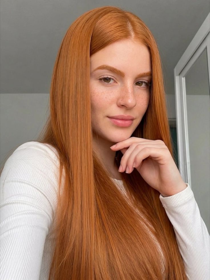 Woman with long red hair and freckles wearing a white shirt indoors