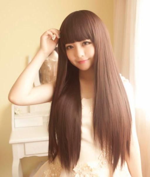 Woman with long brown hair and bangs wearing a white dress indoors