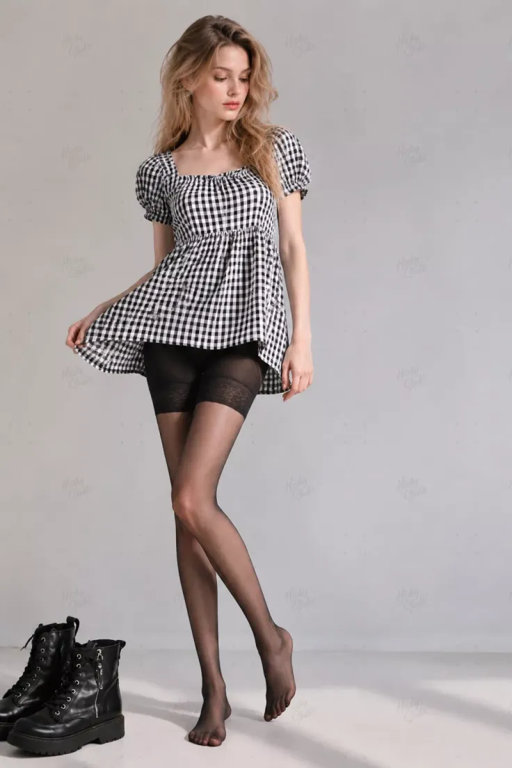 Woman in a gingham dress and black tights with black boots on the floor