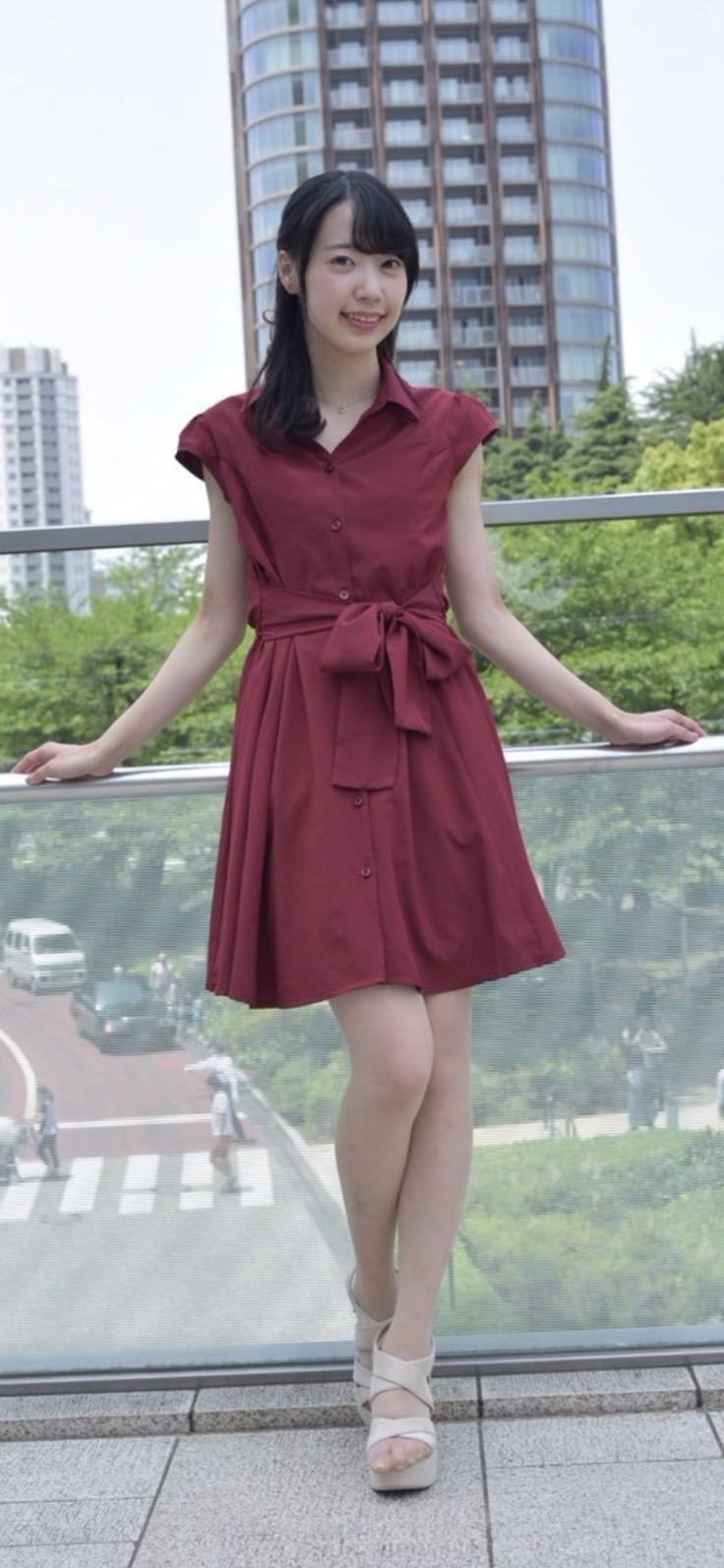 Woman in a red dress standing on a bridge overlooking a city street