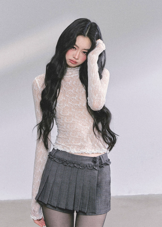 Woman with long dark hair wearing a lace top and pleated skirt indoors