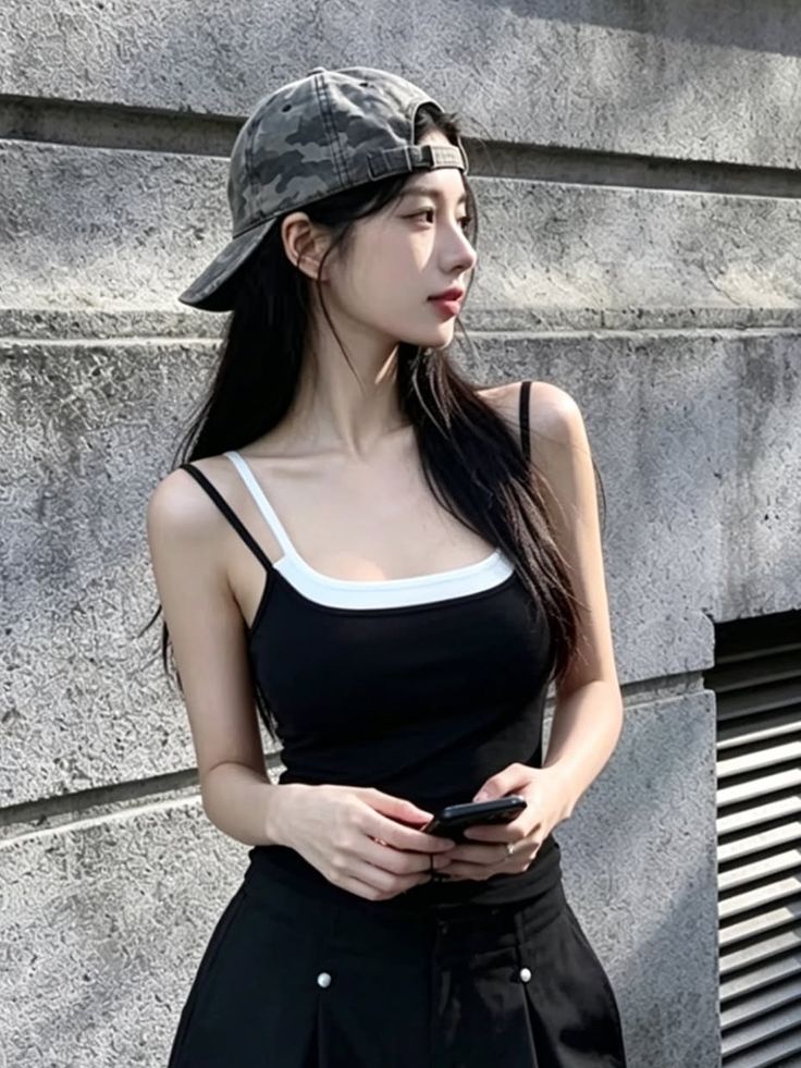 Woman in a black tank top and camo cap holding a phone outdoors