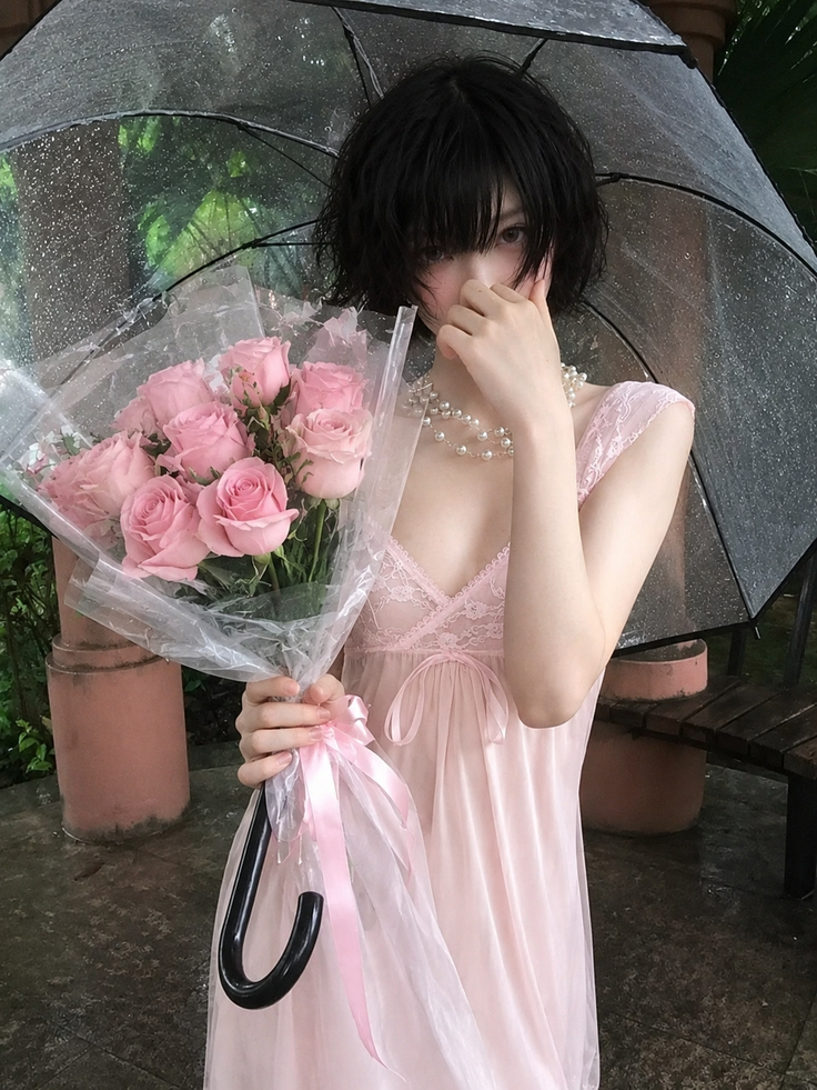 Person in a pink nightgown holding pink roses and an umbrella on a rainy day