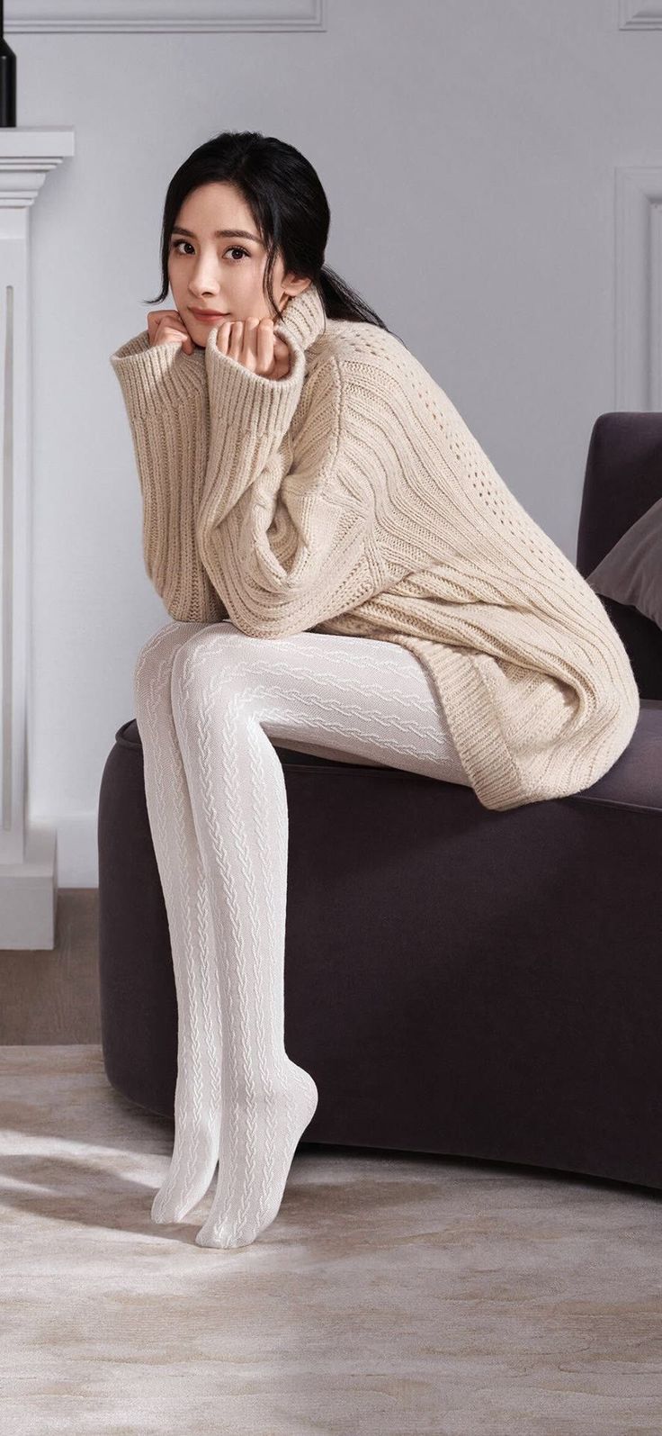 Woman in a beige turtleneck sweater and white tights sitting indoors