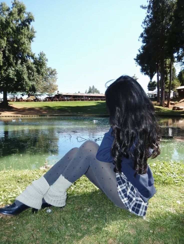 Person with long black hair sitting by a lake on a sunny day