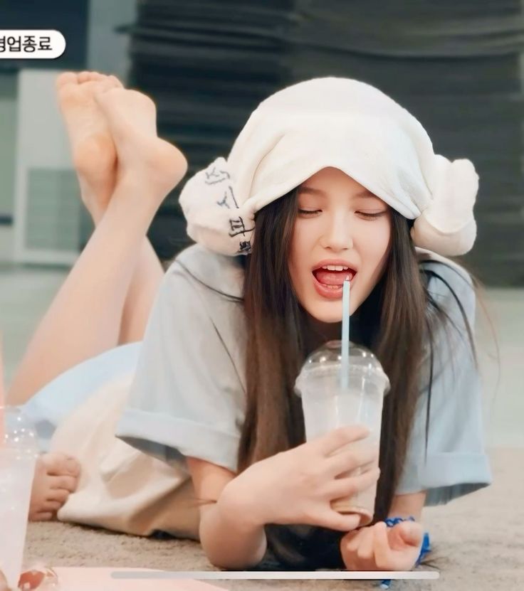 Person with long hair and a white hat lying down and drinking from a straw