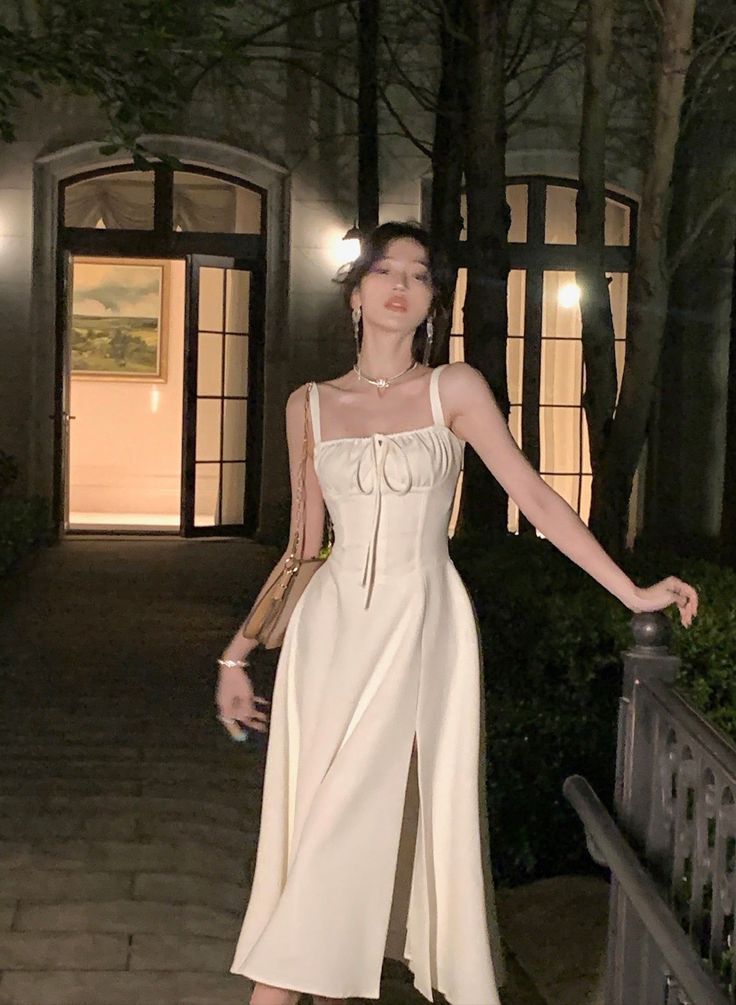 Woman in a white dress with a slit standing outdoors at night