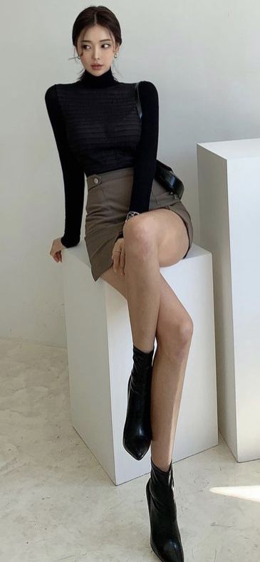 Woman in a black turtleneck and mini skirt sitting on a white cube
