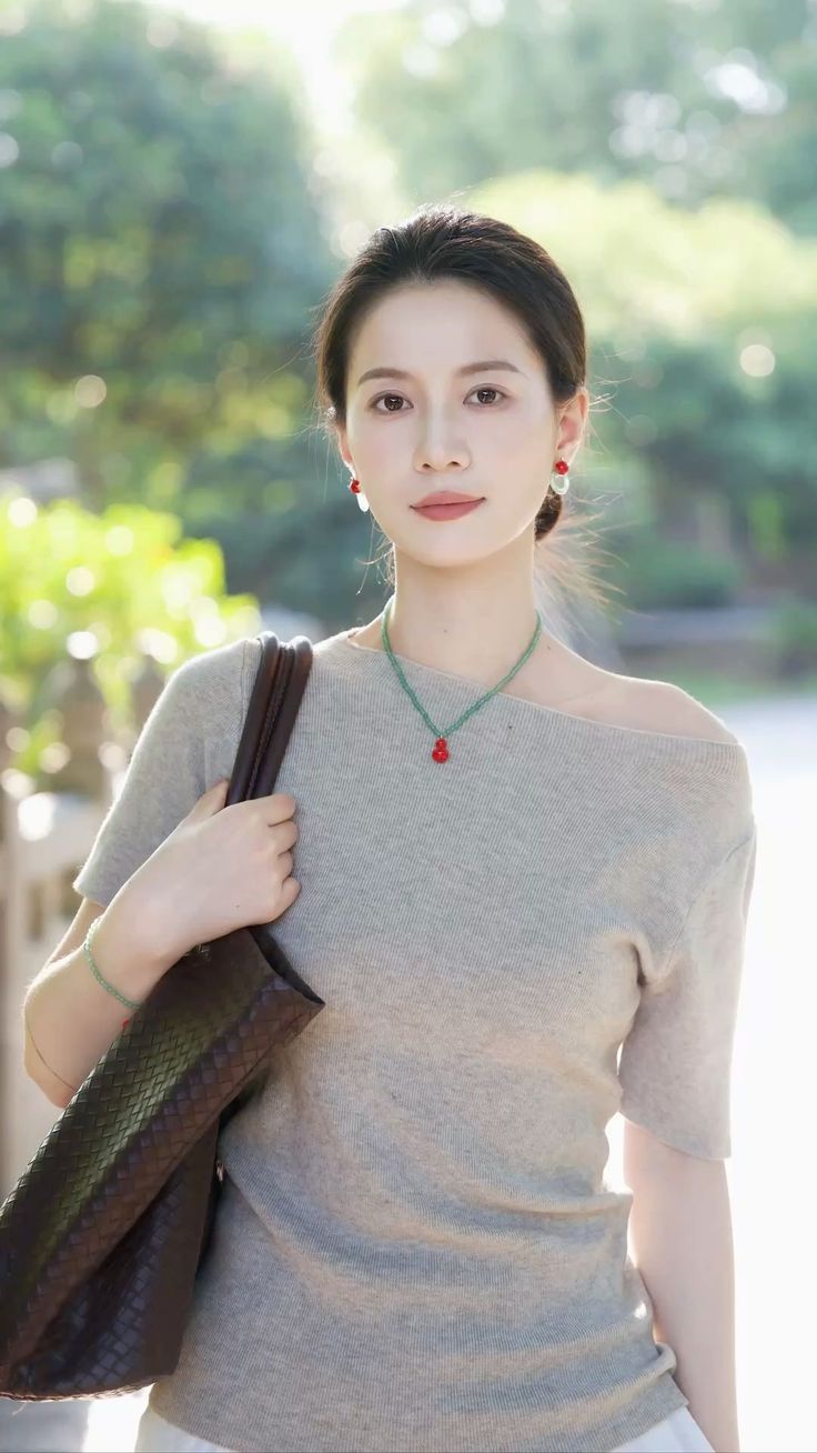Woman in an off-shoulder top with a brown bag and red earrings outdoors
