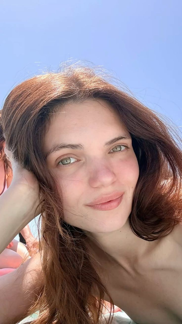 Woman with long brown hair and green eyes outdoors in bright sunlight