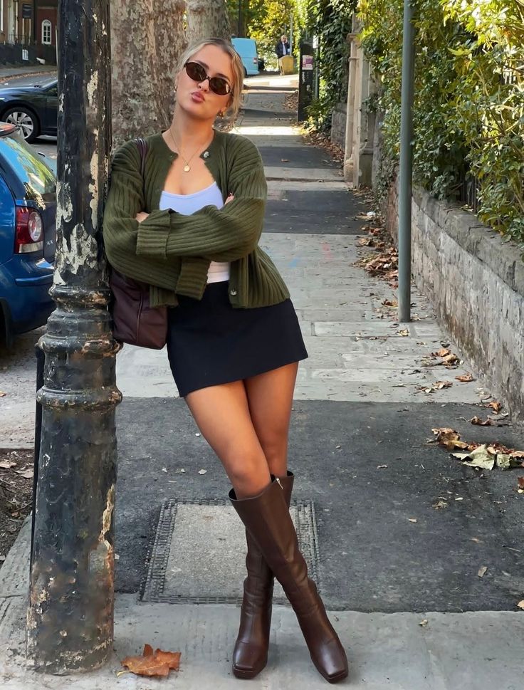 Woman in a green cardigan and mini skirt posing on a sidewalk