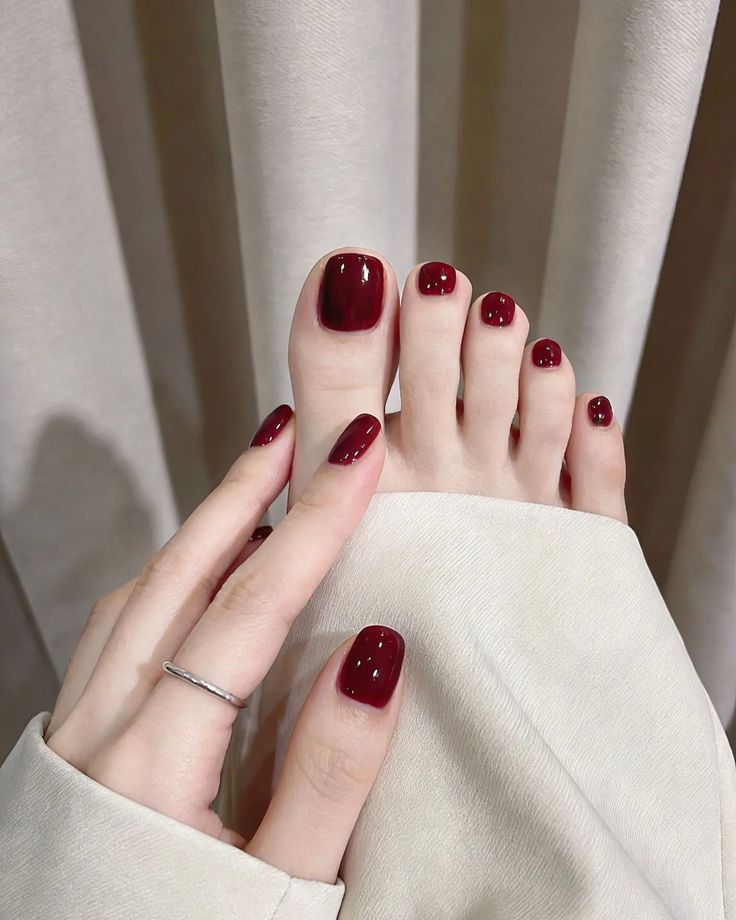 Hand touching a foot, both with glossy red nail polish
