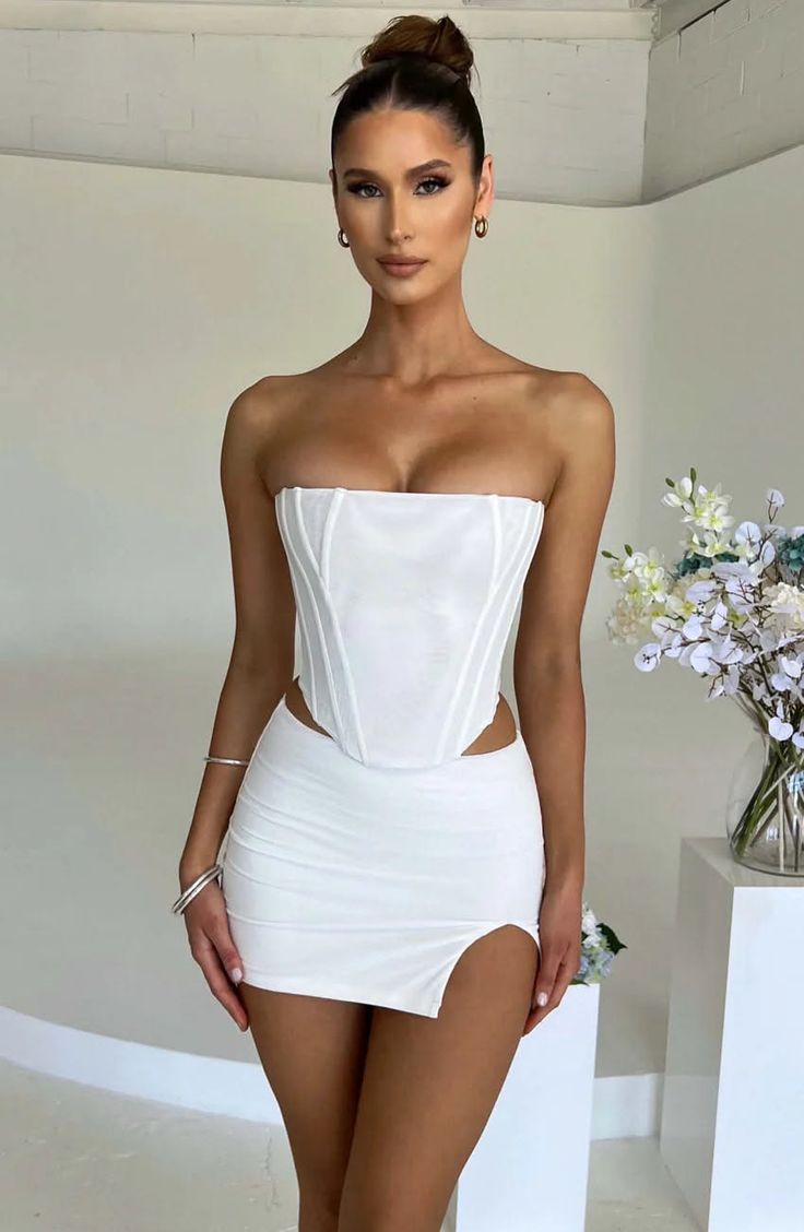 Woman in a white corset and mini skirt with an updo hairstyle indoors