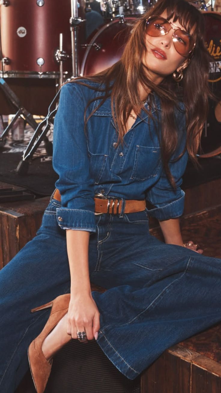 Woman in a denim jumpsuit and sunglasses sitting in front of a drum set