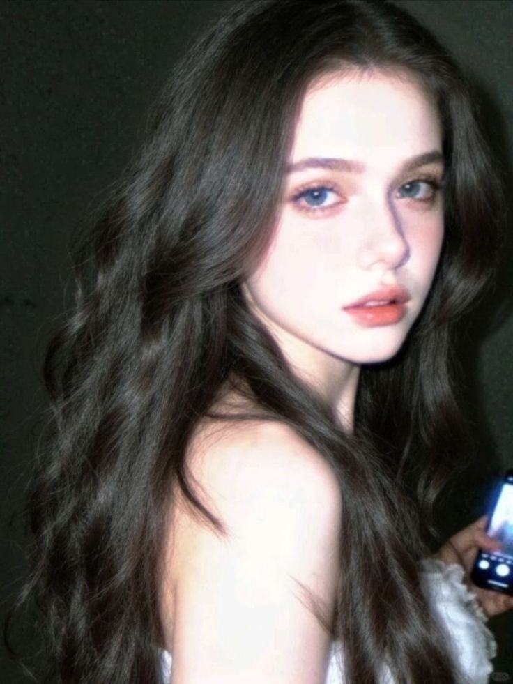 Woman with long dark hair and blue eyes holding a phone
