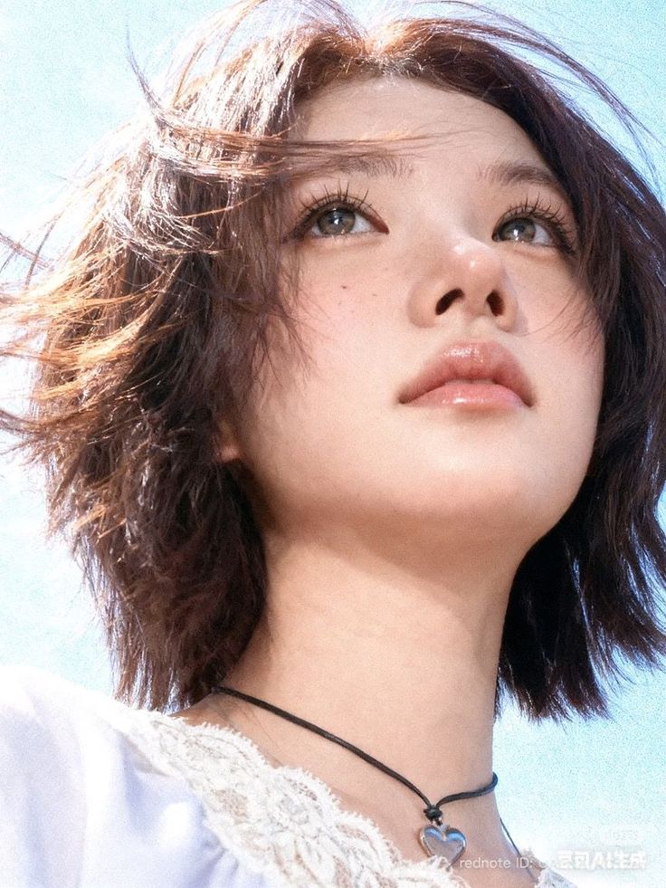 Woman with short brown hair and freckles looking up against a bright blue sky