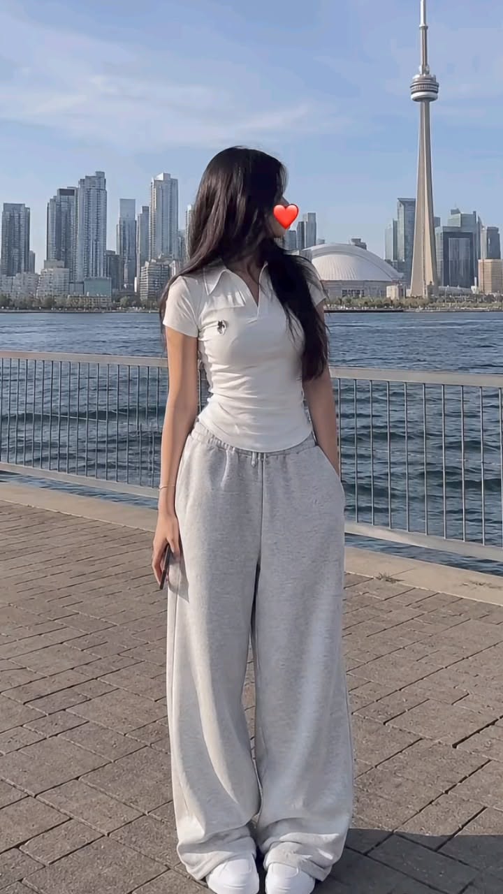Woman in a white polo shirt and grey sweatpants by the waterfront with a cityscape