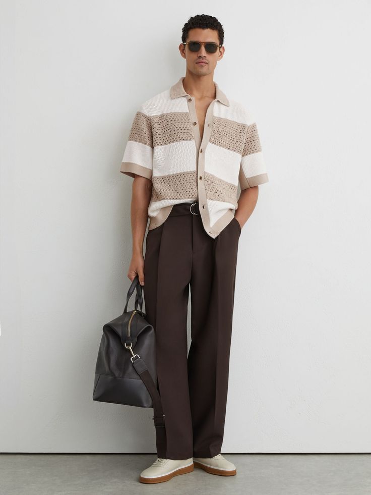 Man in a striped shirt and brown pants holding a black duffel bag