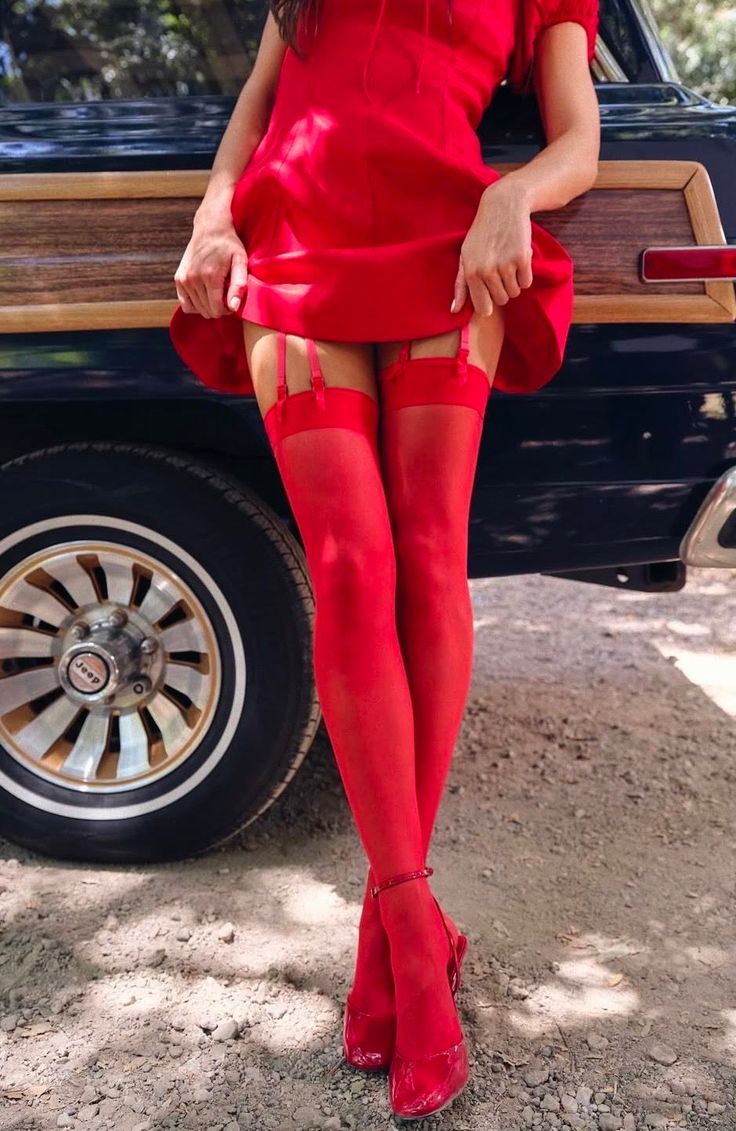 Woman in a red dress and stockings leaning against a vintage car
