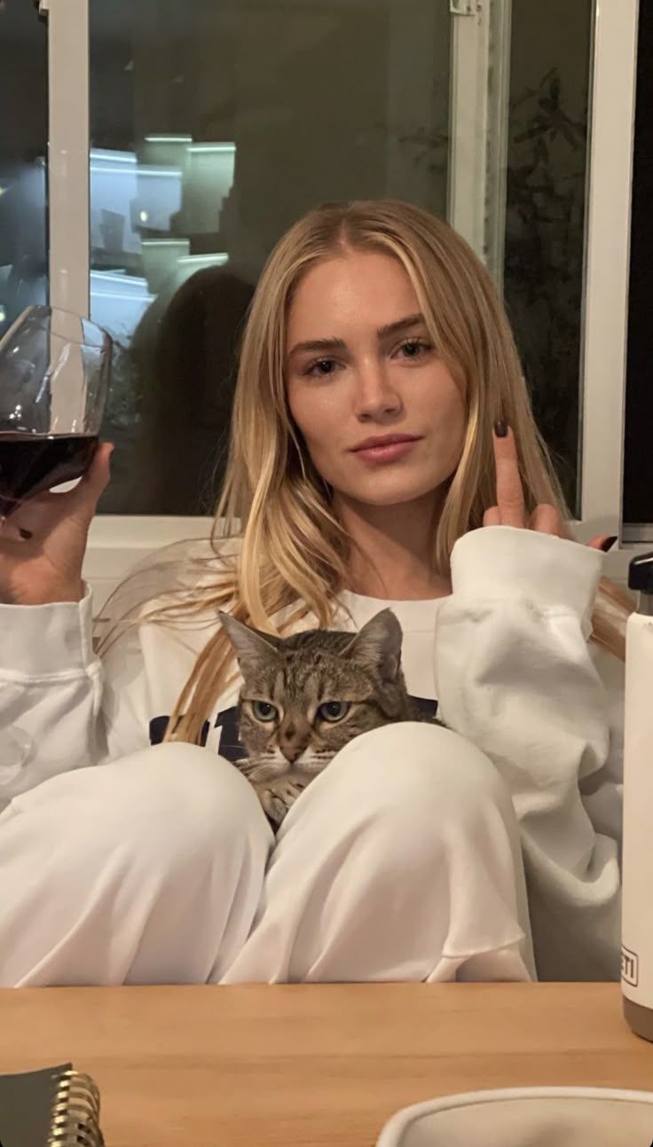 Blonde woman holding a wine glass and a cat, making an offensive gesture