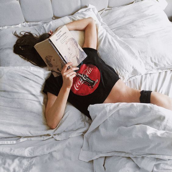 Woman lying in bed reading a book, wearing a black t-shirt and underwear