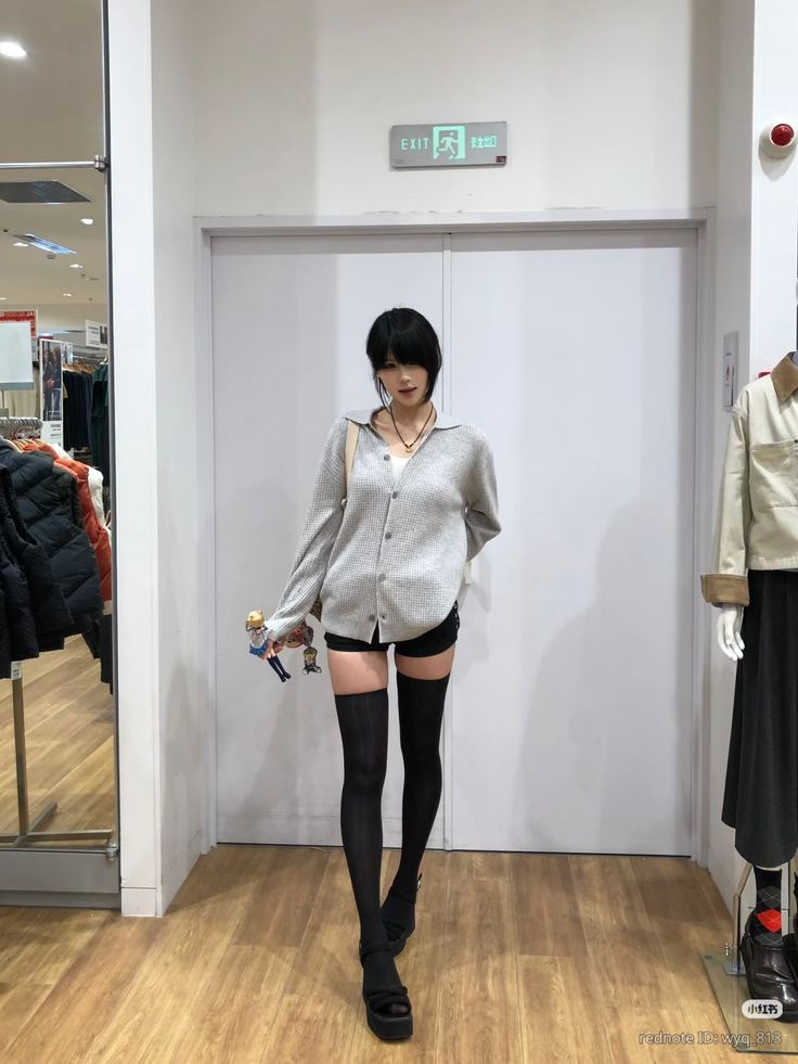 Woman in a grey cardigan, black shorts, and thigh-high socks indoors