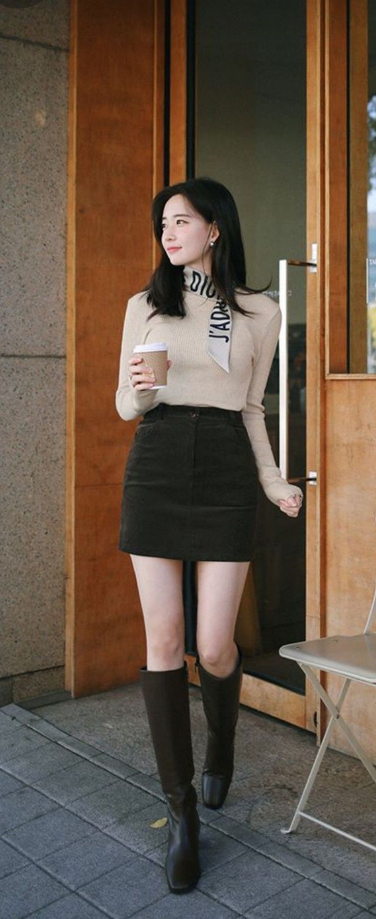 Woman in a beige top and black mini skirt holding a coffee cup outdoors